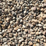 A close-up view of many small, smooth, multicolored pebbles and stone fragments spread out, forming a natural, textured surface.