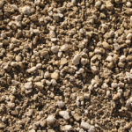 A close-up view of loose, dry, and unevenly sized clumps of brown soil mixed with small rocks and the occasional stone, filling the entire frame.