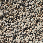 A close-up view of a large pile of small, irregularly shaped, light gray and beige stone gravel, densely packed together.