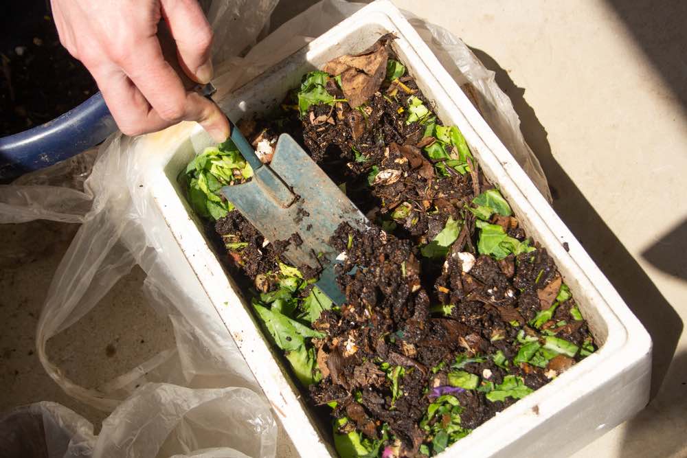 adding compost to your garden from a compost bin